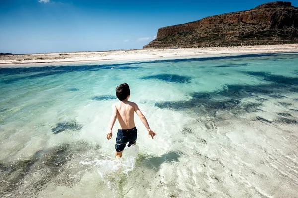 Pojke i badbyxor stående i vatten vid stranden — Stockfoto