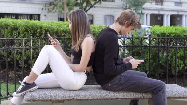 Joven pareja adolescente ignorándose entre sí usando sus teléfonos inteligentes — Vídeos de Stock