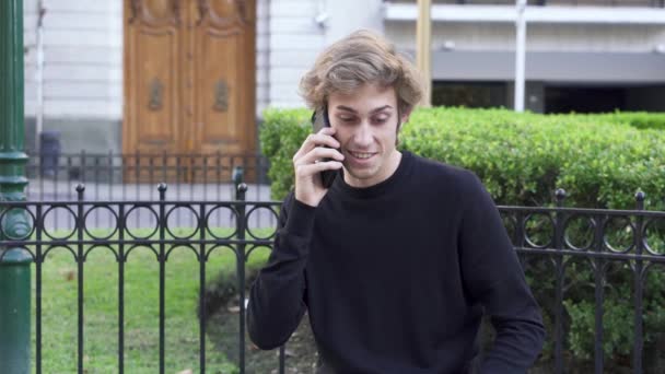 Teen αγόρι μιλάει στο τηλέφωνο σε εξωτερικούς χώρους σε ένα παγκάκι σε ένα τετράγωνο — Αρχείο Βίντεο