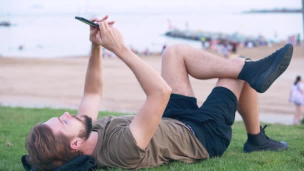 Młody człowiek zrelaksowany przy użyciu smartfona i na czacie na plaży — Wideo stockowe