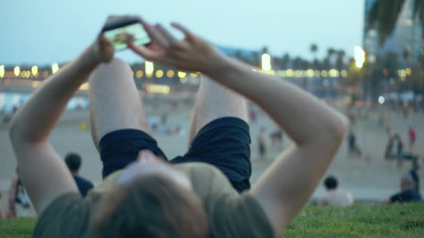 Jongeman ligt te bladeren op het sociale netwerk op het strand — Stockvideo