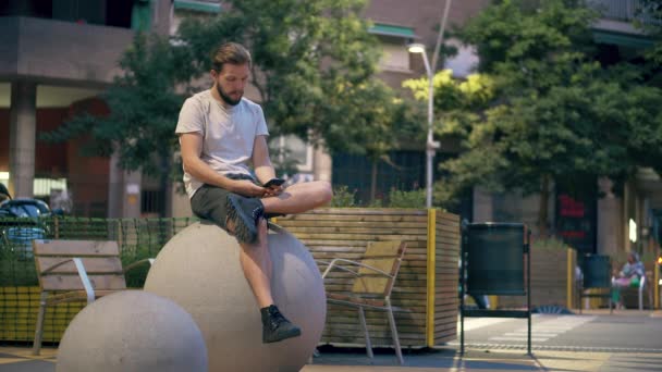 Ung man som använder smartphone på torget på kvällen — Stockvideo