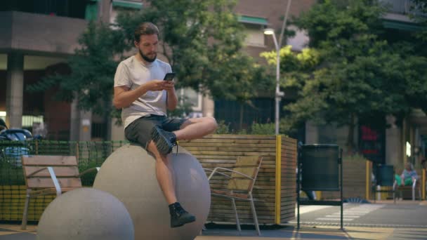 Mladý muž s vousy pomocí smartphone na náměstí ve večerních hodinách — Stock video