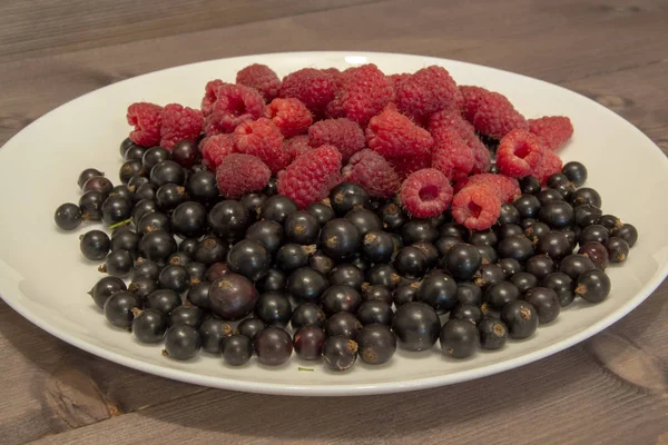 Arándanos y frambuesas en un plato sobre una mesa de madera — Foto de Stock