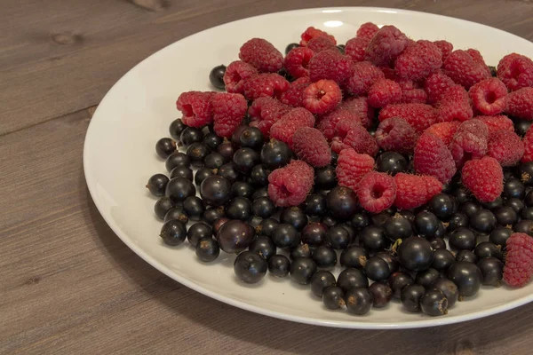 Myrtilles et framboises dans une assiette sur une table en bois — Photo