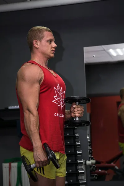 Spor salonunda dumbells ile yakışıklı kaslı genç adam eğitim. S