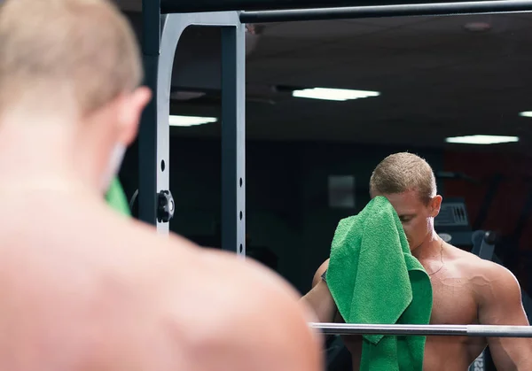 Young muscular man in the gym wipes his face with towel standing