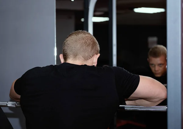 Genç kas adam spor salonunda aynaya bakıyor, gri üzerinde yalın