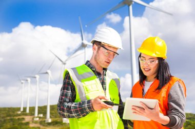 Young workers looking and checking wind turbines at field clipart