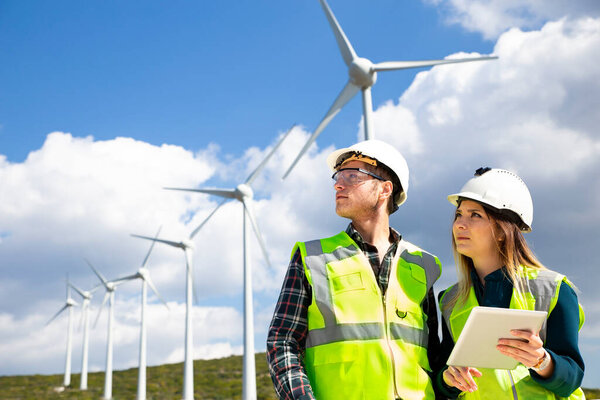 Young workers looking and checking wind turbines at field