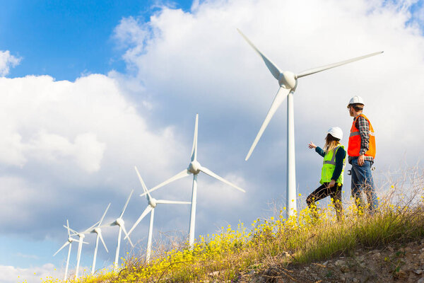 Young engineers looking and checking wind turbines at field