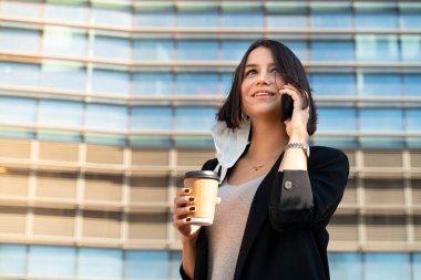 Maskesini takan kadın kahve içerken telefonla konuşuyor.