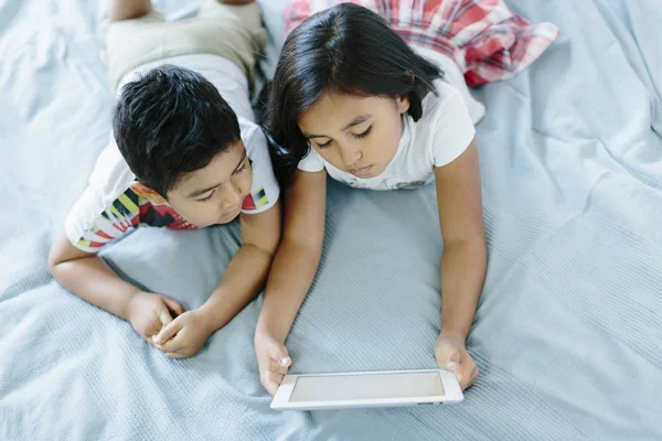 Two siblings lying on bed using a tablet