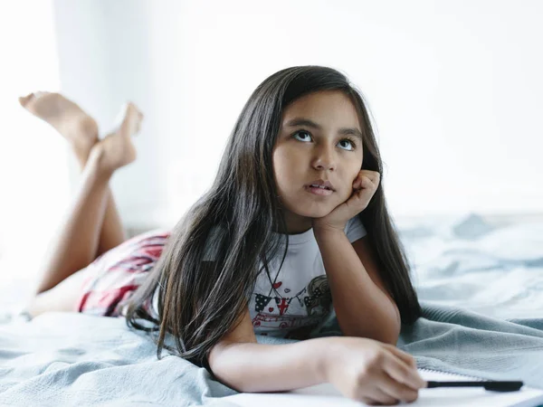 Jong meisje liggend op bed opzoeken. — Stockfoto