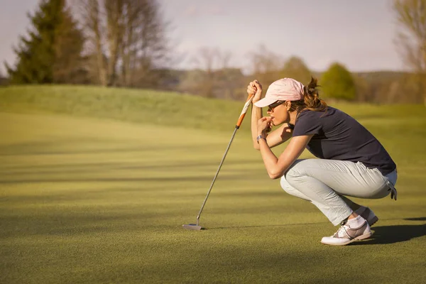 Yeşil üzerinde kadın golf oyuncusu çömelme.