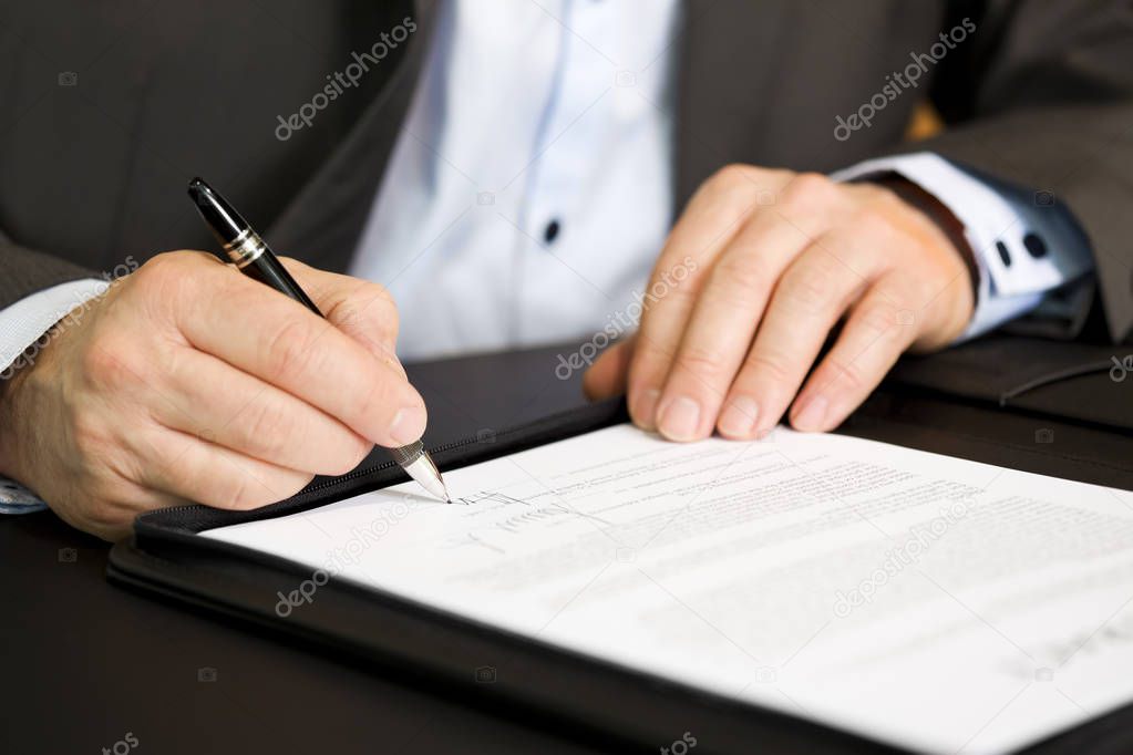 Business person signing a contract, focus on signature.