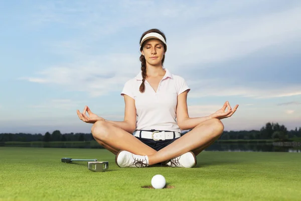 Kız golfçü golf sahasında yoga duruş oturan.