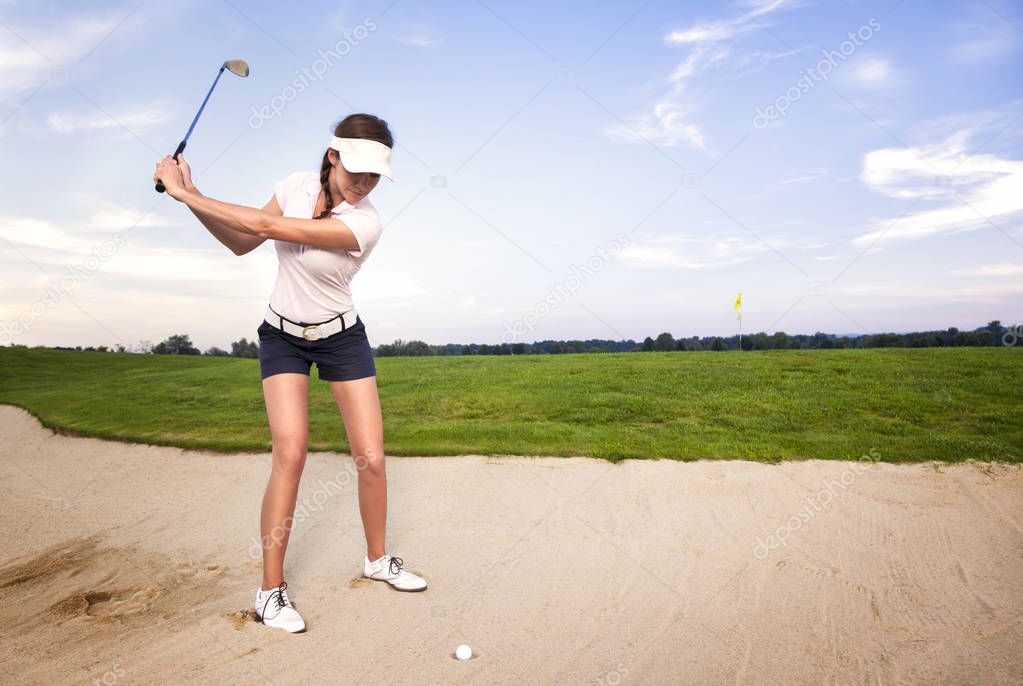 Woman golf player in sand trap preparing to hit the ball.