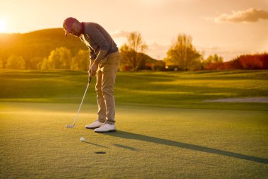 Erkek golf oyuncusu gün batımında koyarak.