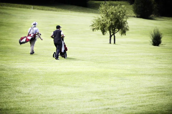 Mężczyźni chodzą na polu golfowym z torbami. — Zdjęcie stockowe