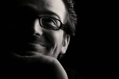 Yakın çekim genç gülümseyen adam avuç içi yukarı bakan çene dinlenme, düşük anahtar, siyah ve beyaz