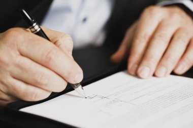 Ofis masasında oturan bir işadamı imzaya odaklı bir sözleşme imzalıyor..