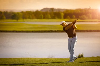 Erkek üst düzey golf oyuncusu copyspace ile gün batımında arka planda göl ile golf kulübü sallanan.