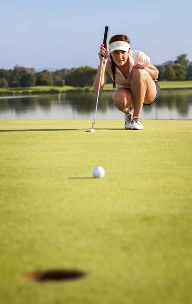 女高尔夫球手蹲下分析绿色把高尔夫球放进洞里 — 图库照片