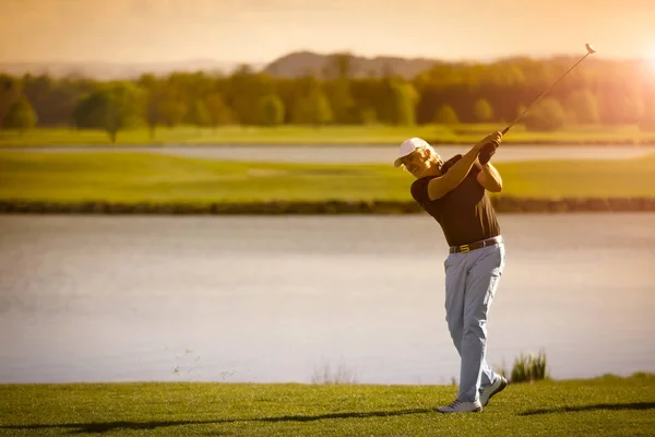 Erkek üst düzey golf oyuncusu copyspace ile gün batımında arka planda göl ile golf kulübü sallanan.