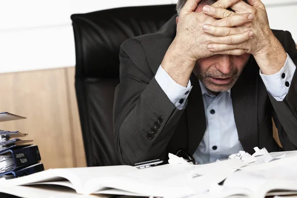 Endişeli işadamı kitap ve evrak iş ile aşırı dolu ofis masasında oturan.