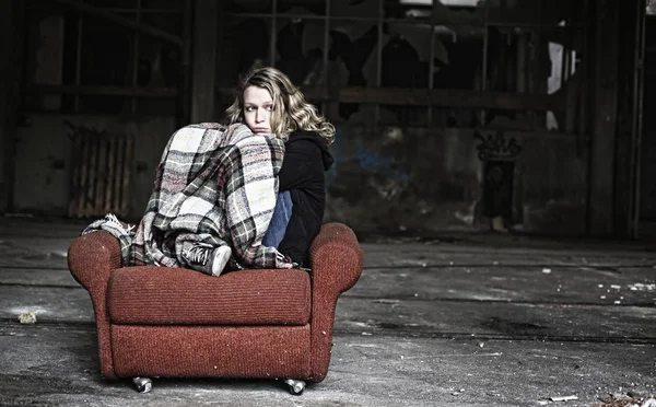 Sad woman sitting on shabby red sofa being covered with old blanket.