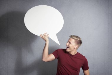 Büyük haber: Neşeli yakışıklı adam gri arka plan üzerinde izole metin için alan ile beyaz boş konuşma balonu tutan.