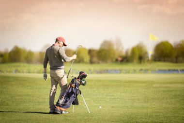 Erkek golf oyuncusu çanta dan golf kulübü dışarı alarak, arka planda yeşil ve bayrak ile.