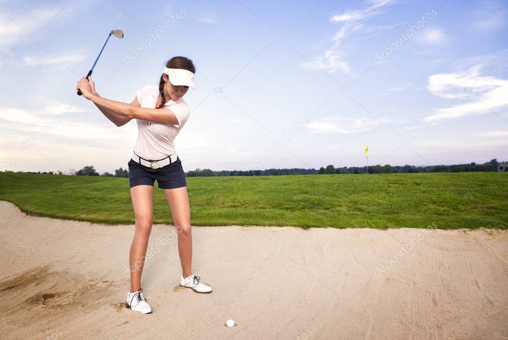 Girl golfer preparing for chipping the ball out of the sand trap.