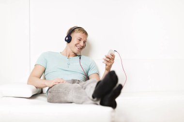 Young man listening music with headphones and resting on couch.
