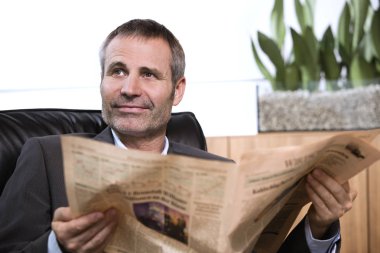 İşadamı gazete okuyor ve yukarı bakıyor.