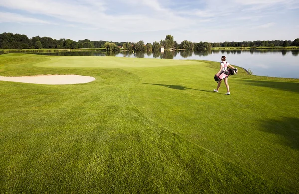 Kız golfçü golf çantası ile golf sahasında yürüyüş.