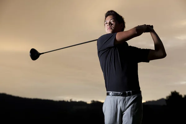Jogador de golfe teeing off ao pôr do sol . — Fotografia de Stock
