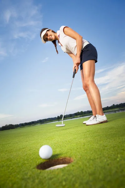 Glückliche Golferin steckt Ball in Loch. — Stockfoto