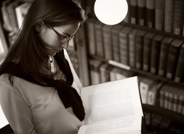 Student reading at bookshelf, B&W — ストック写真