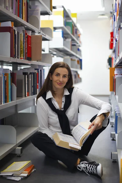 Studentin sitzt zwischen Bücherregalen und liest — Stockfoto