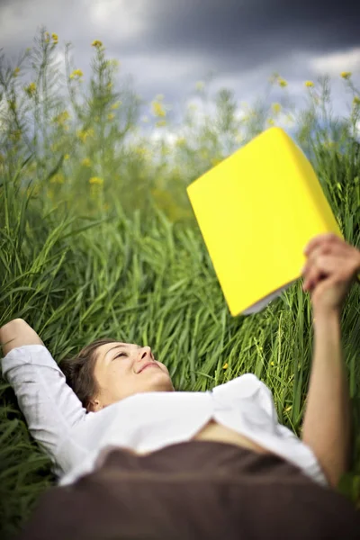 Kobieta leżąca na polu rzepaku czytająca — Zdjęcie stockowe