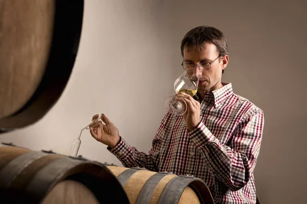 Winemaker tasting wine in cellar.