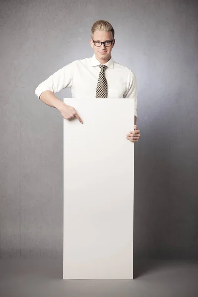 Amistoso hombre de negocios señalando con el dedo a la cartelera vertical en blanco — Foto de Stock