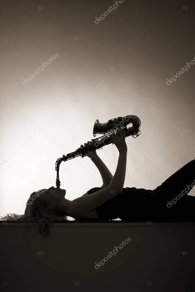 Silhouette of woman playing saxophone, sepia toned.