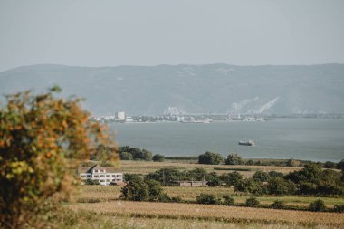 Büyük kargo gemisinin bulunduğu manzara, güneşli yaz günlerinde Sırbistan 'ın tepeleriyle birlikte Sırbistan' ın Sırbistan sınırındaki Tuna Nehri üzerindeki sanayi limanına geliyor.