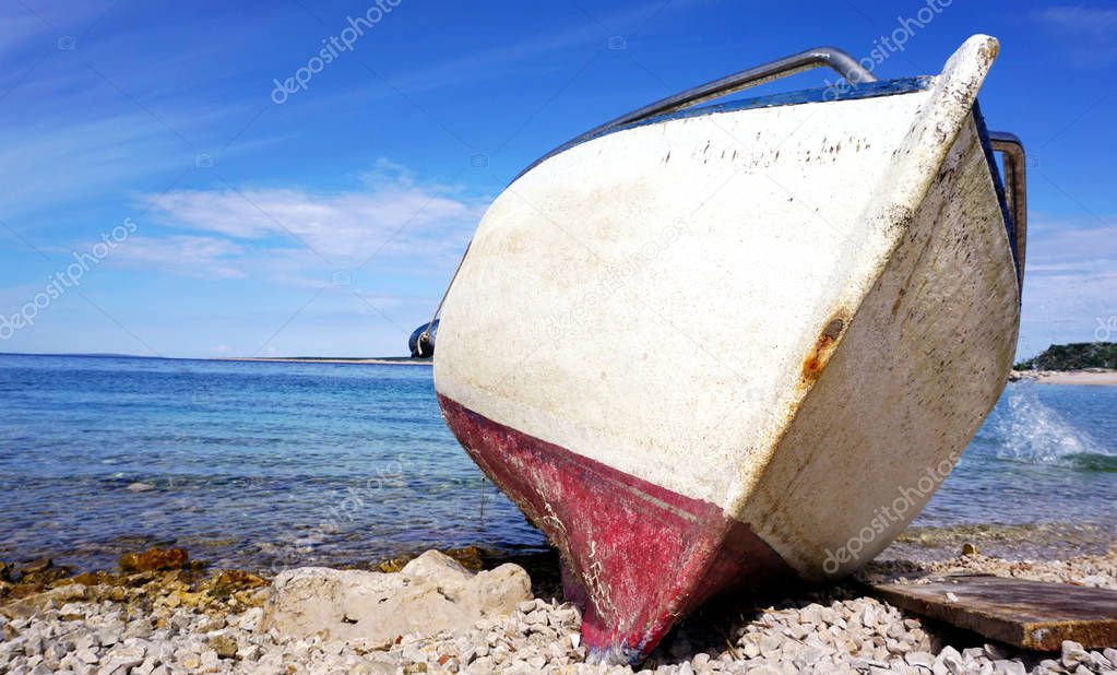 Bow of old damage boat stranded on the pebble beach with blue sea and sky in the background