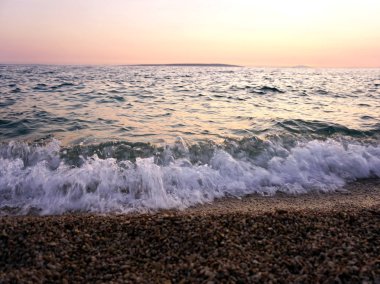 Gün batımında deniz kıyısında gelgit dalgaları ve deniz köpüğü ve çakıl plajı