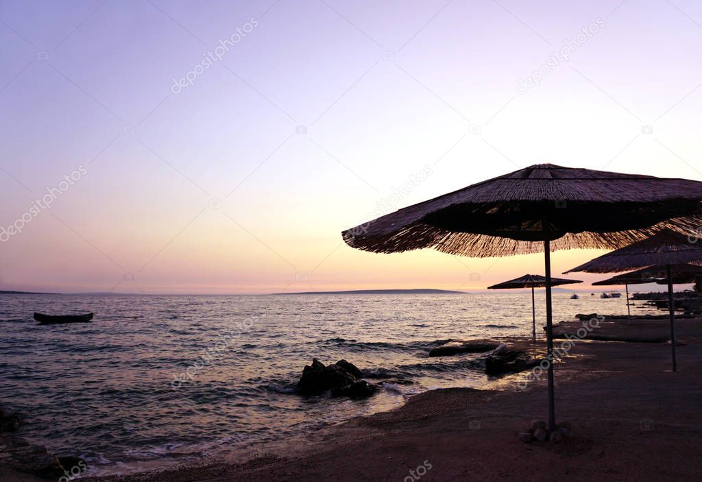 Bamboo sun umbrellas on the empty beach by the sea on the sunset, with pastel color sky and sea