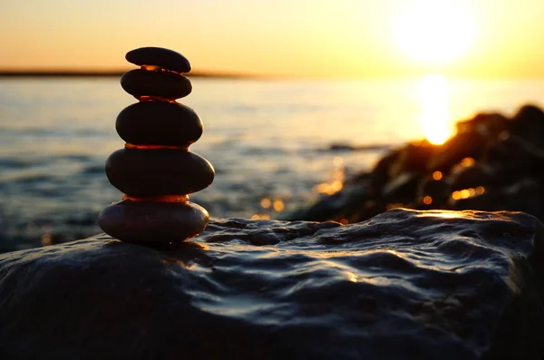 Summer sea sunset background with pebble beach and stacking stones silhouette in front of the sun